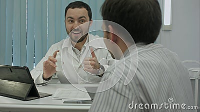 Male bearded doctor in clinic advertises preparation to client. Stock Photo