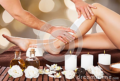 Male beautician waxing woman's leg in spa Stock Photo