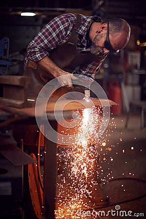 Male Blacksmith Using Plasma Cutter To Cut Shape From Sheet Metal In Forge Stock Photo