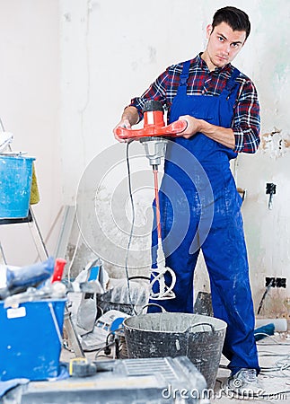 Builder mixing plaster in bucket with electric mixer Stock Photo