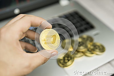 Male businessman hand holding Dash coin on a background of laptop keyboard and pile of golden coins. Virtual money and Editorial Stock Photo