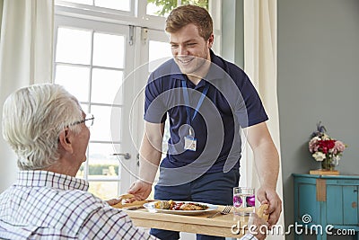 Male care worker serving dinner to a senior man at his home Stock Photo