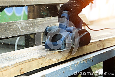 A male carpenter plans boards with an electric planer to make a bench. Carpentry, industry. Woodworker Stock Photo