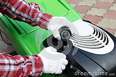 Male Checking the fuel level in lawn mower. A green lawnmower. Gardening. Maintenance of equipment Stock Photo