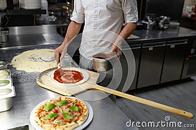 Male chef spreading tomato paste on pizza base Stock Photo