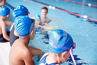 Male Coach In Water Giving Group Of Children Swimming Lesson In Indoor Pool Stock Photo