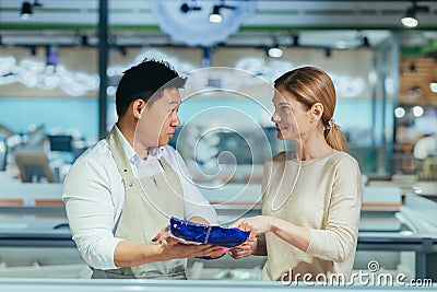 a male consultant in a grocery store advises a woman talking to assistant. seller at vegetable market help customer in Stock Photo