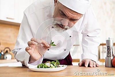 Male cook chef decorating garnishing prepared salad dish on the plate in restaurant commercial kitchen. Stock Photo