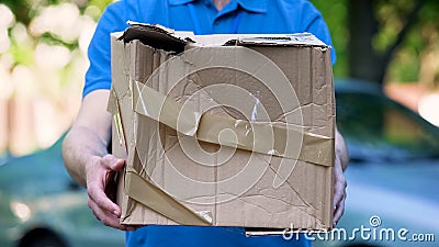 Male courier showing damaged box, cheap parcel delivery, poor shipment quality Stock Photo