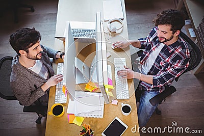 Male coworkers smiling while working at computer desk Stock Photo
