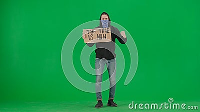 A male demonstrator with his face covered by a scarf holds up a sign that says Time is now. The man demonstrator on a Stock Photo