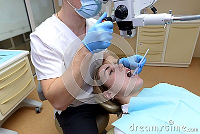 Dentist examines a young beautiful woman, looks at her teeth with a professional microscope in a surgical dental office Stock Photo