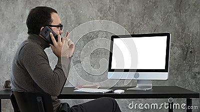 Male Designer Working At Computer In Contemporary Office. He talks on the phone and looking on what is on the screen Stock Photo