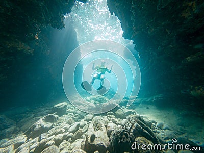 Male diver swimming through natural underwater tunnel. Stock Photo