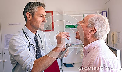 Male doctor checking senior male patient mouth with otoscope Stock Photo