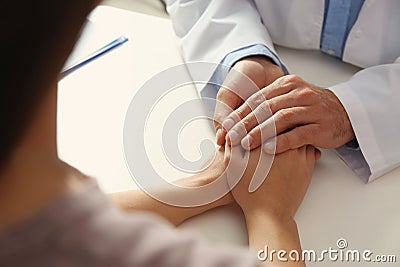 Male doctor comforting woman at table, closeup of hands. Stock Photo