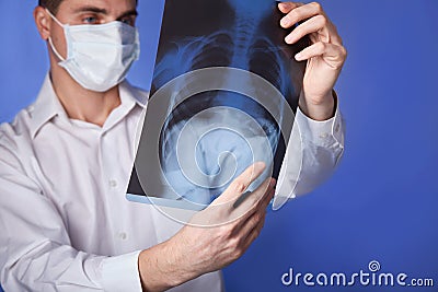 Male doctor in mask and white coat holding x-ray or roentgen of lungs, fluorography, image on blue background Stock Photo