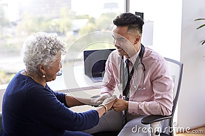 Male Doctor In Office Reassuring Senior Female Patient And Holding Her Hands Stock Photo