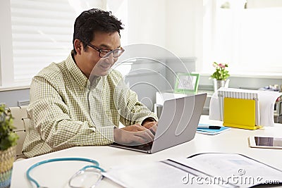 Male Doctor Sitting At Desk Working At Laptop In Office Stock Photo