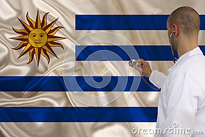 Male doctor with a stethoscope on the background of the silk national flag of Uruguay, the concept of medical care, quarantine, Stock Photo