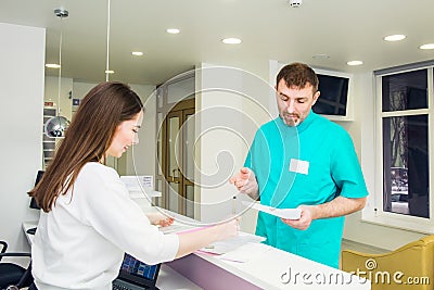 Male doctor talking and discuss working shedule with young friendly female receptionist at hospital reception desk. Occupation, st Stock Photo
