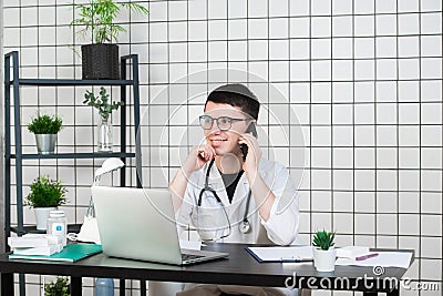 Male doctor using telephone while working on computer at table in clinic Stock Photo