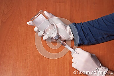 Male doctors hands in rubber gloves holding syringe and bottle of liquid drugs on wooden table.Concept sterility purity Stock Photo