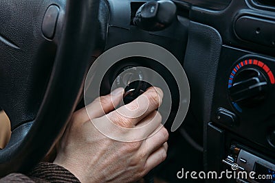 Male driver hand inserts key in ignition lock to start car Stock Photo