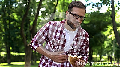 Male eating burger, feeling nausea, junk food poisoning, body intoxication Stock Photo