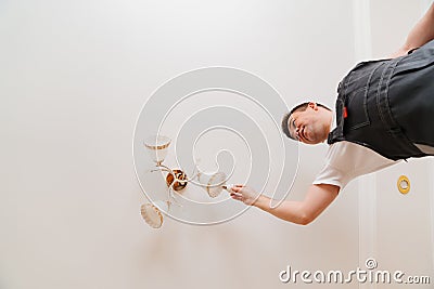 A male electrician changes the light bulbs in the ceiling light. Stock Photo