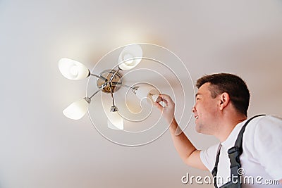 A male electrician changes the light bulbs in the ceiling light. Stock Photo