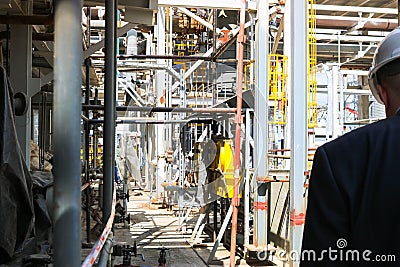 A male engineer manager in a white construction helmet walks through an oil refinery chemical metallurgical plant with equipment Editorial Stock Photo