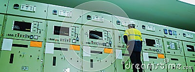Male engineer wearing a yellow uniform and wearing a white safety hat, inspecting electrical systems in a large power plant Stock Photo