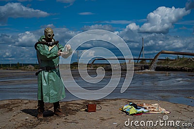 A male environmentalist in a green protective suit and gas mask takes a sample of water in a polluted lake for research Stock Photo