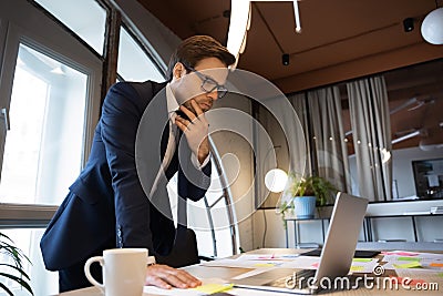 Male executive standing by table studying data on laptop screen Stock Photo