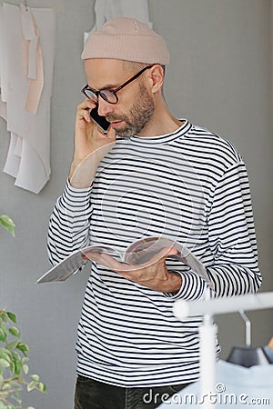 male fashion designer or fashion designer flips through a magazine and talks on the phone with a client. an adult Stock Photo