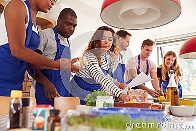 Male And Female Adult Students Looking At Recipe In Cookery Class In Kitchen Stock Photo