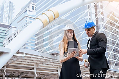 Male and female industrial engineers holding a tablet and blueprints working and discussing on building site Stock Photo