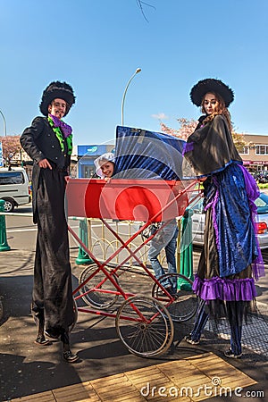 Two stilt walkers and a very tall baby carriage Editorial Stock Photo