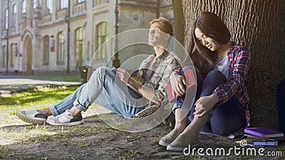 Male and female strangers sitting under tree, first meeting, indecisiveness Stock Photo