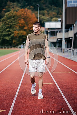 Male figure striding confidently across an orange running track in a stadium setting Stock Photo