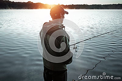 A male fisherman on the lake is standing in the water and fishing for a fishing rod. Fishing hobby vacation concept. Copy space Stock Photo