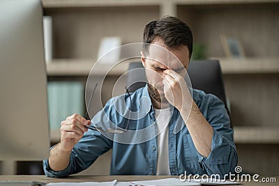 Male Freelancer Suffering Eyes Strain, Taking Off Glasses And Massaging Nose Bridge Stock Photo