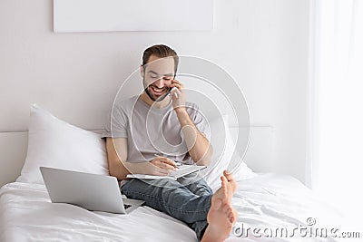 Male freelancer talking on phone while working in bed Stock Photo