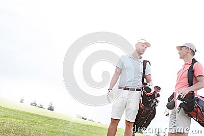 Male friends conversing at golf course against clear sky on sunny day Stock Photo