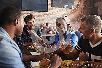 Male Friends Eating Out In Sports Bar With Screens In Behind Stock Photo