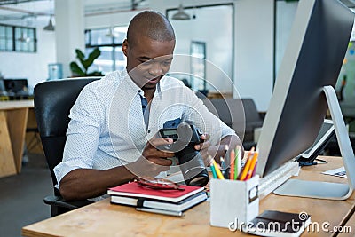 Male graphic designer reviewing captured images in his digital camera at desk Stock Photo
