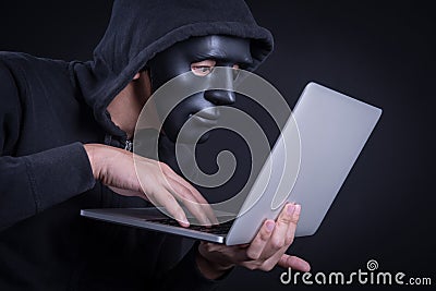 Male hacker with black mask carrying laptop Stock Photo