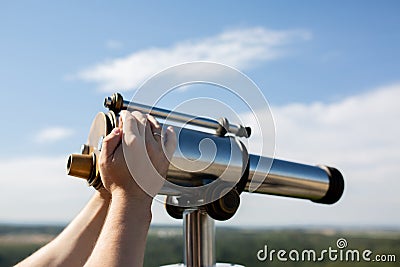 Male hand adjusts sharpness on a touristic binocular against forest panorama Stock Photo