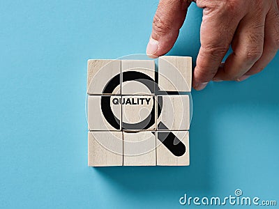 Male hand arranging wooden cubes with a magnifier focusing on the word quality. Quality control, searching for best quality Stock Photo